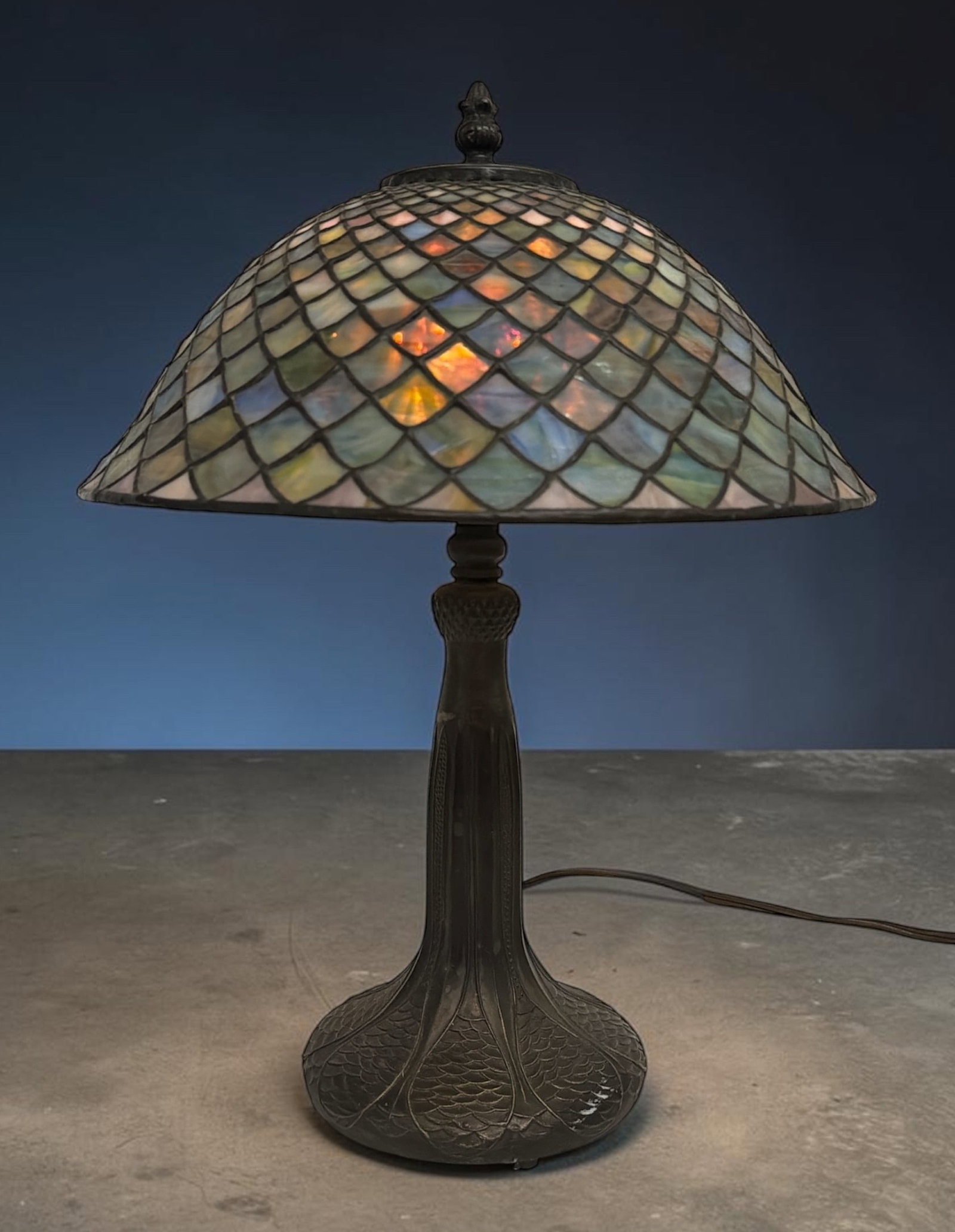 An Antique After Tiffany Stained Glass Lamp: Measures 16" H x 12" shade diameter, 6" base diameter. Fish Scale pattern.