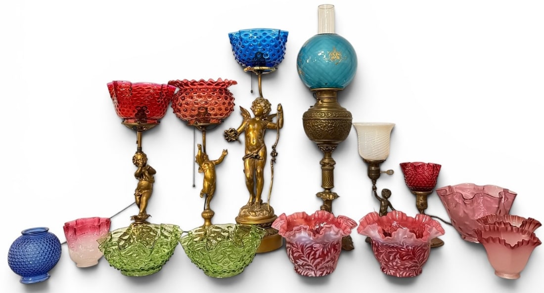 Collection of French Cherub Lamps, Art Glass Shades: Includes two small gold-toned metal cherub lamps with ruby red glass shades, a larger bronze cherub lamp after Auguste Moreau with a blue glass shade, a blue glass and gold painted shaded oil lamp, a 