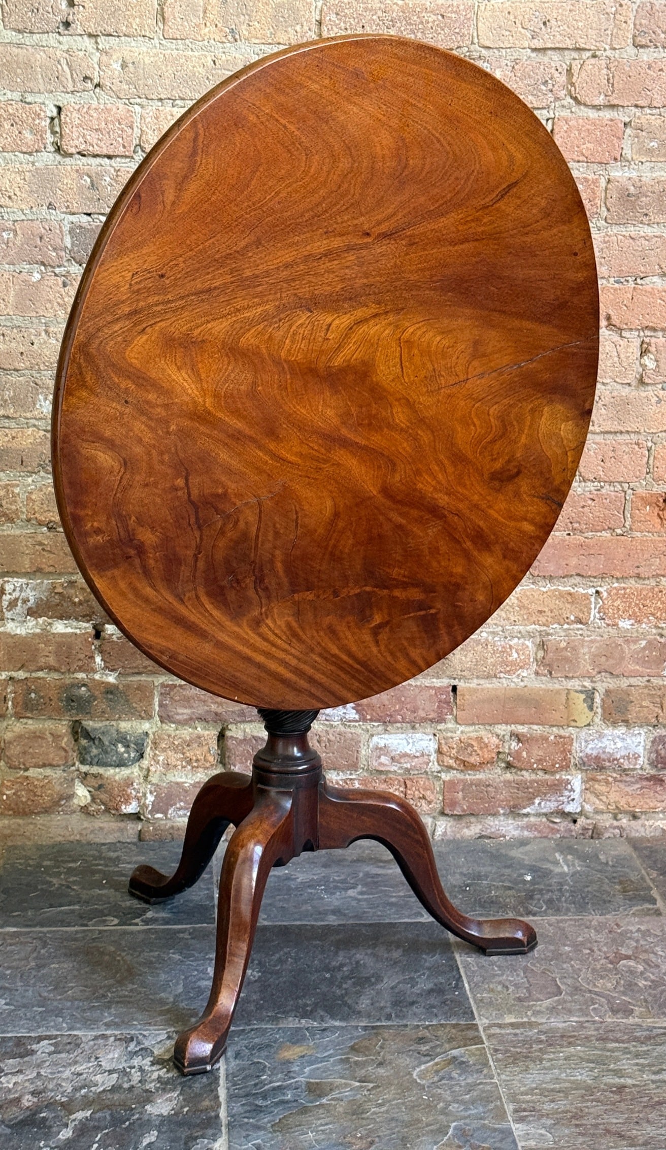 18th C. Georgian Flamed Mahogany Tilt Top Table: Mahogany tilt top table with snake feet and turned wood base. Measures 29" H x 30.5" diameter.