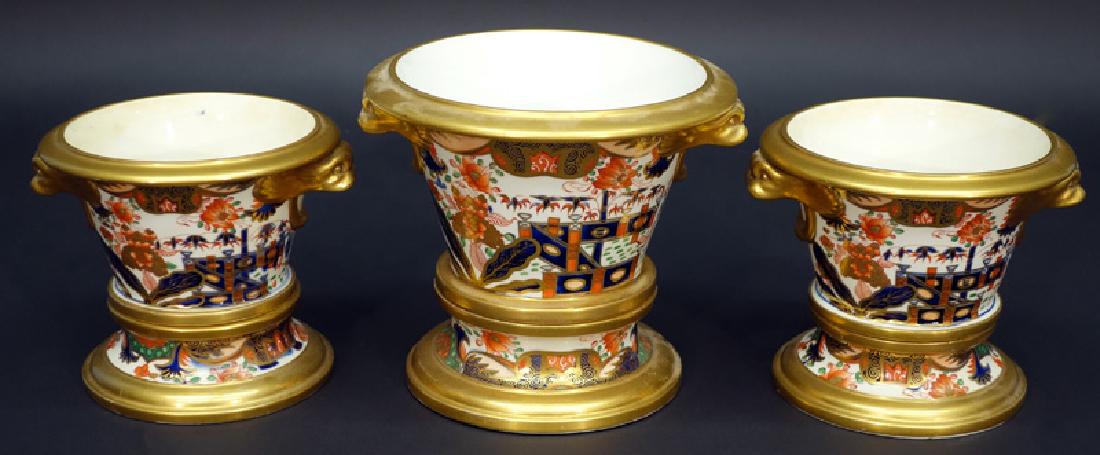 FLOWER POTS (3): Unmarked Derby or Worcester; painted porcelain; gilt decorated trim and dolphin handles; floral motif; sit on separate bases for water drainage; largest has crack in base, (2) minor hairlines; H-5"-6"