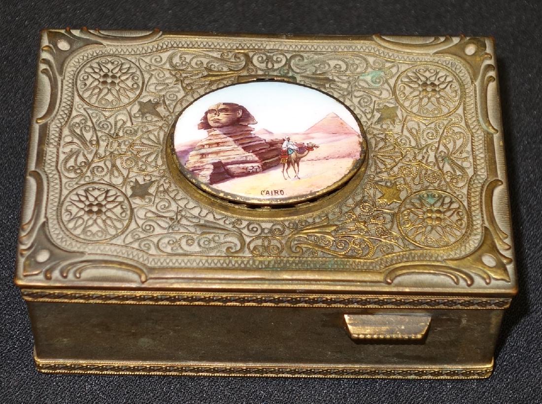 MUSICAL BIRD BOX: Bronze with Egyptian enamel oval scene; bird has feathers; will wind and bird will pop-up and move wings and mouth; bellows deteriorated and a small interior piece is loose; L-4", F-G