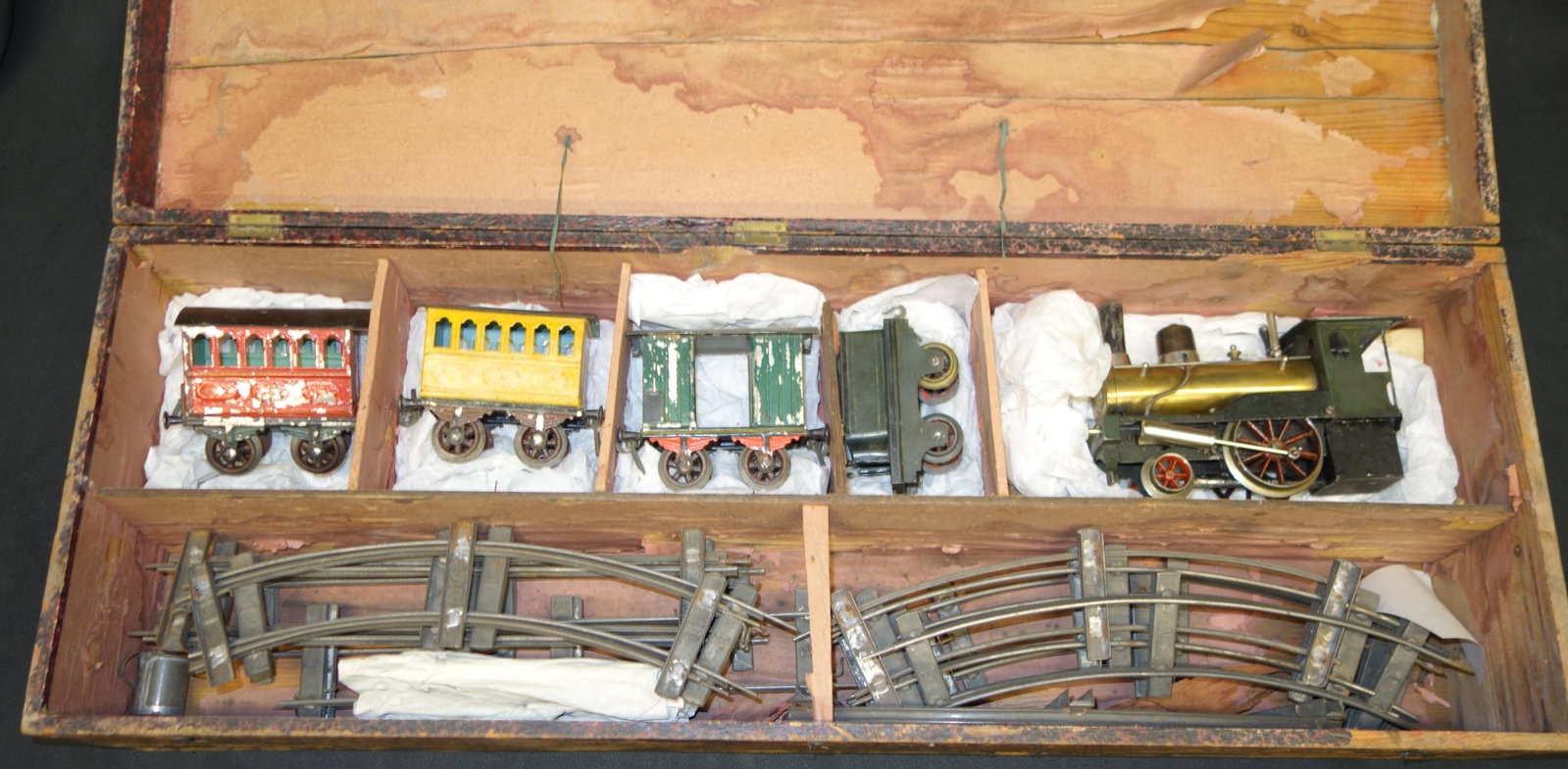 BING STEAM TRAIN SET: 1-gauge; locomotive, tender, (3) cars, track, original wood box with partial paper label; brass and painted tin; has burner; paint flaking, mostly on cars; box L-35", G-VG