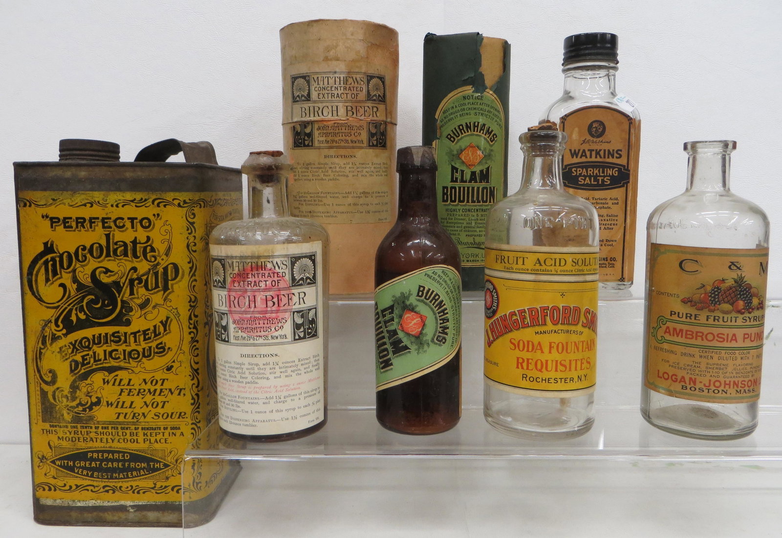 SODA FOUNTAIN SYRUPS, ETC (6): Many with paper labels-("Perfecto"); (1) chocolate syrup tin- ("Perfecto"), rust; (1) Burnhams clam broth bottle with sleeve; (1) Matthews birch beer extract bottle with cardboard container; (1) Hunge
