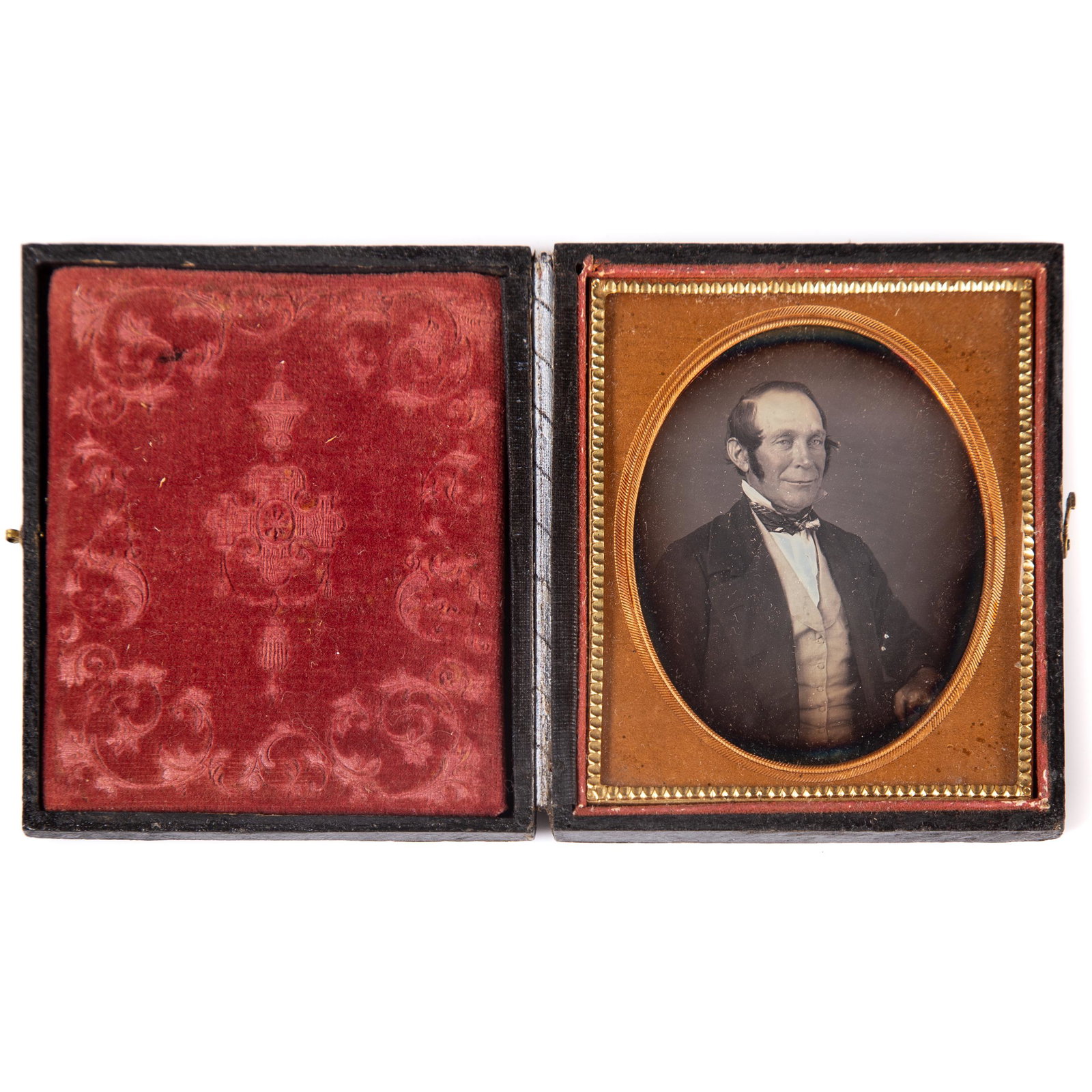 DAGUERREOTYPE IMAGE: Ninth plate; image of grinning man with sideburns wearing vest and light blue tinted shirt; plain gilt mat; stamped leather geometric case; hinge repair with tape; minor case wear and repair, VG-EX