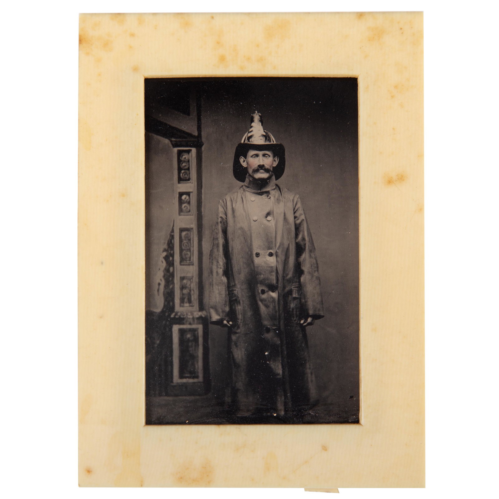 OCCUPATIONAL - FIREMAN TINTYPE: 6th plate; fireman in helmet "1859"; moustache; rouge / tinted cheeks; interesting architectural post; celluloid easel frame; frame 4 1/4" x 3 1/4", VG-EX