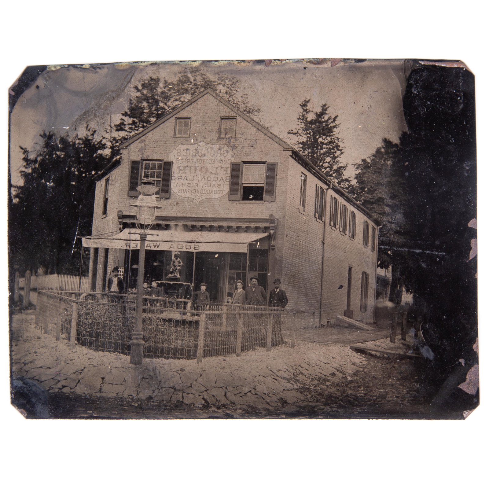 TINTYPE GENERAL STORE: Half plate; image of store with fountain, lamp post and customers in front; products sold listed on sign, including: tobacco, cigars, soda water, etc.; no case; no mat; right side dark; blemishes and 