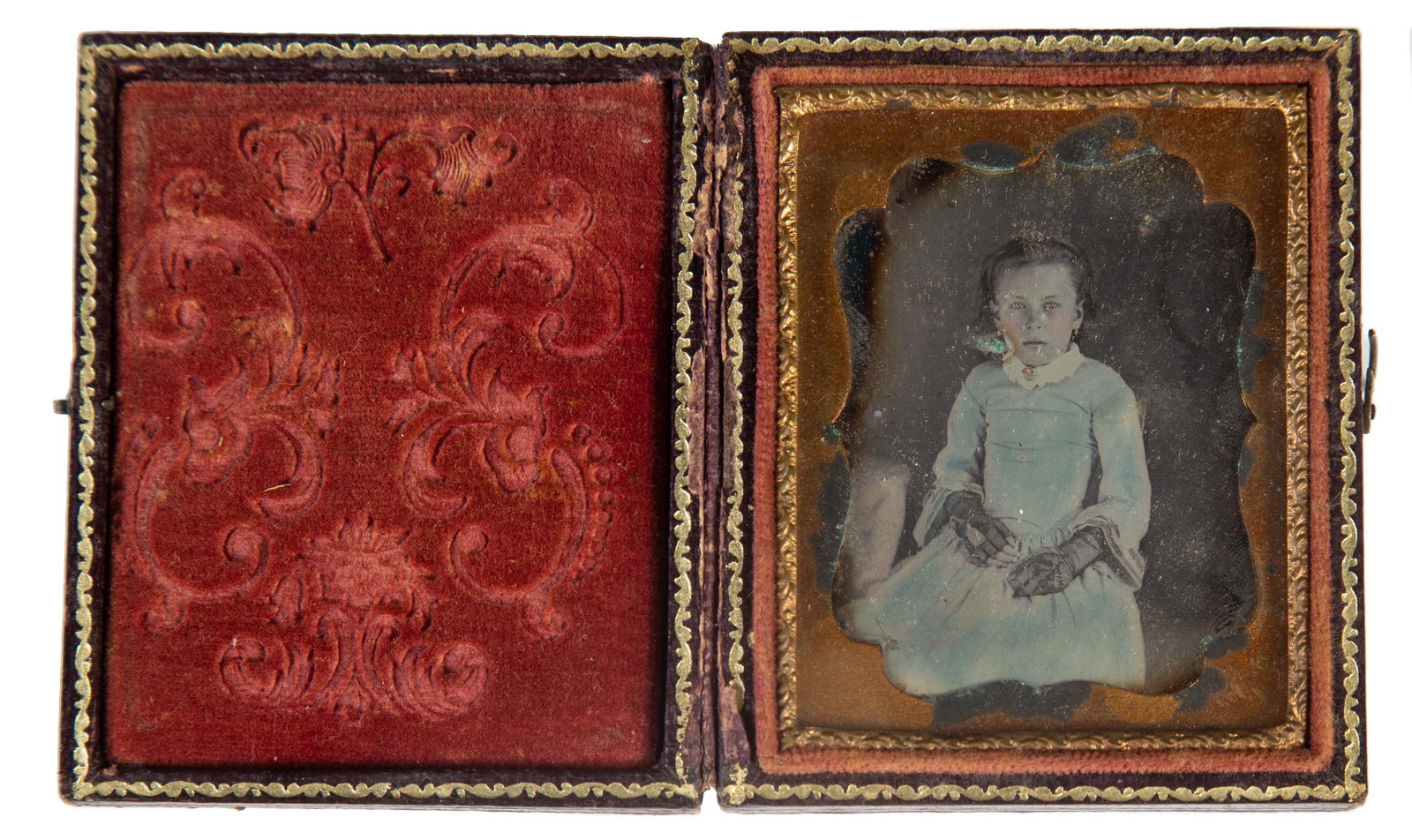 DAGUERREOTYPE OF YOUNG GIRL: 9th plate; image of young girl in blue tinted dress with lace fingerless gloves; gilt metal mat with oxidation in floral stamped leather case with hinge damge; case 3" x 2 1/4", VG