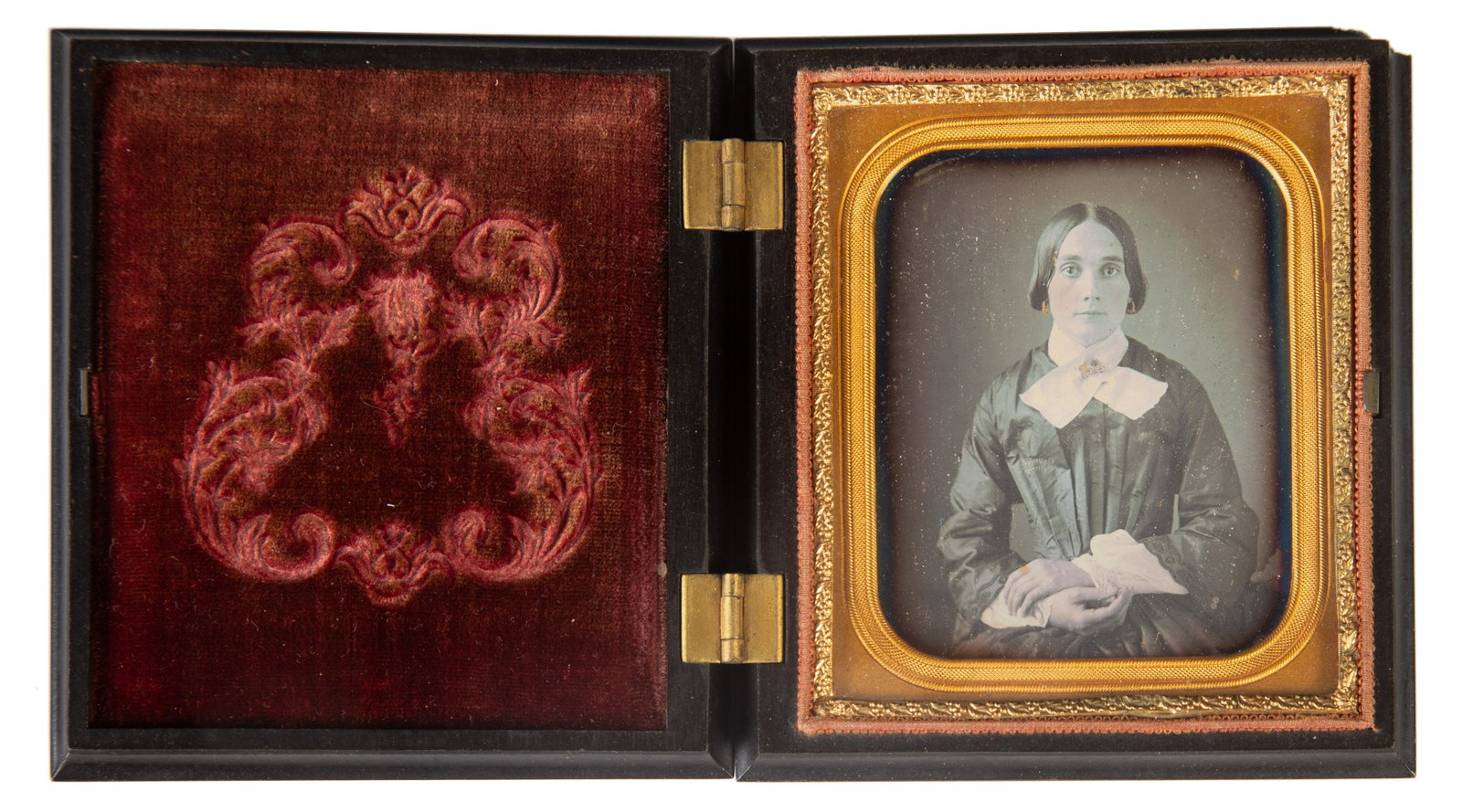 DAGUERREOTYPE PORTRAIT IN GUTTA PERCHA CASE: 6th plate; image of young woman with white collar and cuffs, wearing highlighted earrings and brooch; gilt metal mat; Gutta Percha case; back of case has small geometric pattern with top right upper b