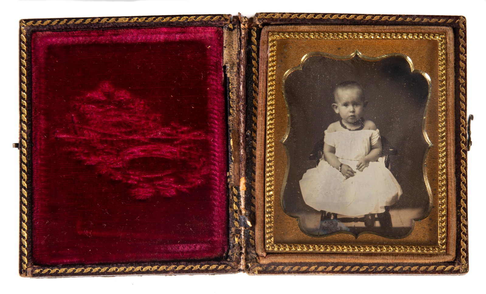 DAGUERREOTYPE OF INFANT: 9th plate; image of infant in white dress, necklace and bracelet; sitting in highchair; gilt mat; simple stamped leather case; minor streaking; case 3" x 2 1/2", VG-EX