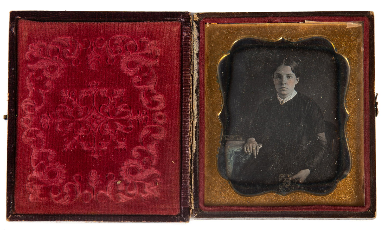 DAGUERREOTYPE PORTRAIT OF YOUNG WOMAN: 6th plate; image of young woman with lace collar, brooch, rings and rouge cheeks; gilt metal mat; foliate stamped leather case with broken hinge; case 3 1/2" x 3", VG-EX