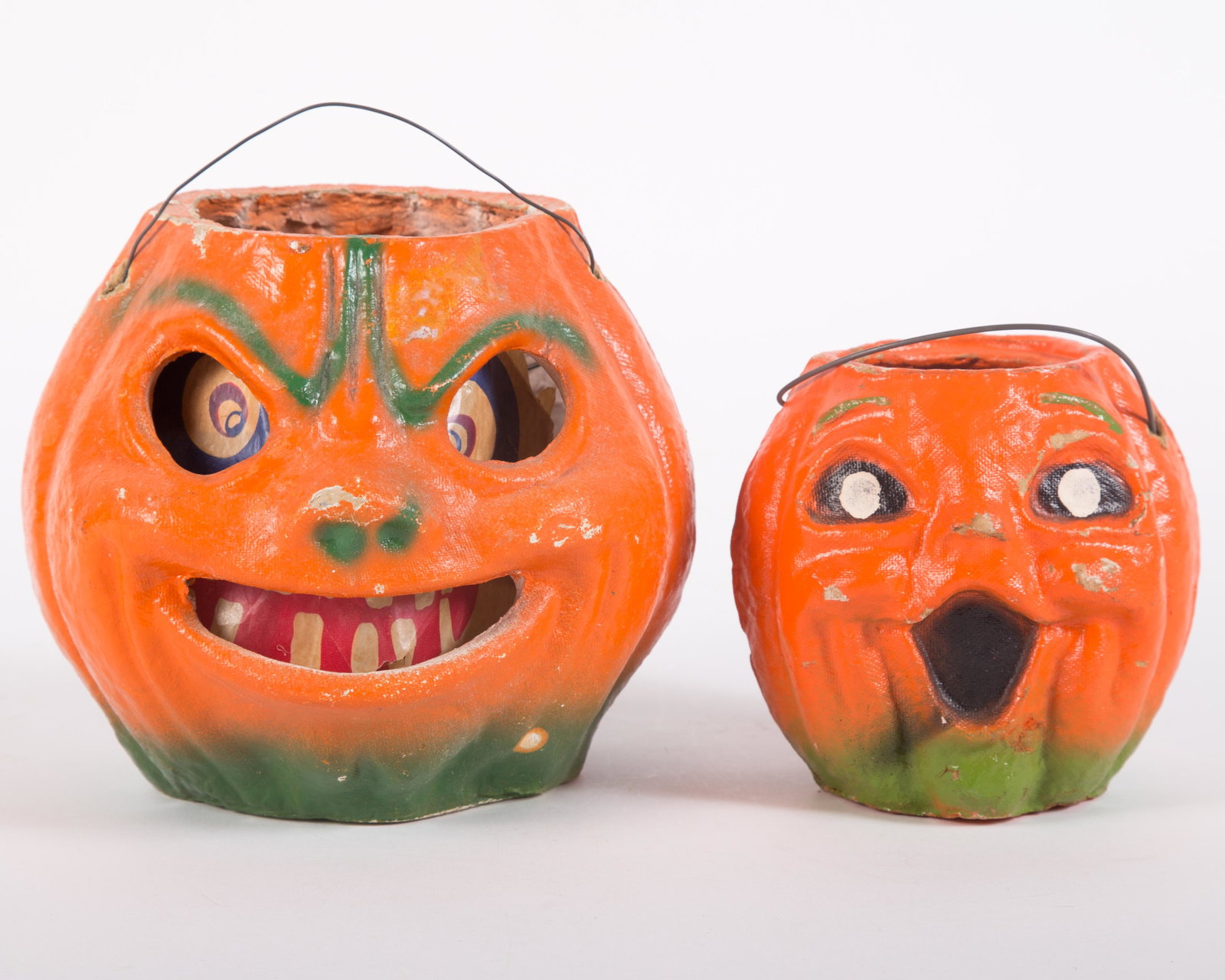 VINTAGE PAPIER MACHE JACK O'LANTERNS (2): Painted papier mache; large one has printed paper insert with reinforced tears; minor paint loss on edges, high spots and handle holes; retains wire handle; smaller has painted face, inpaint on small 
