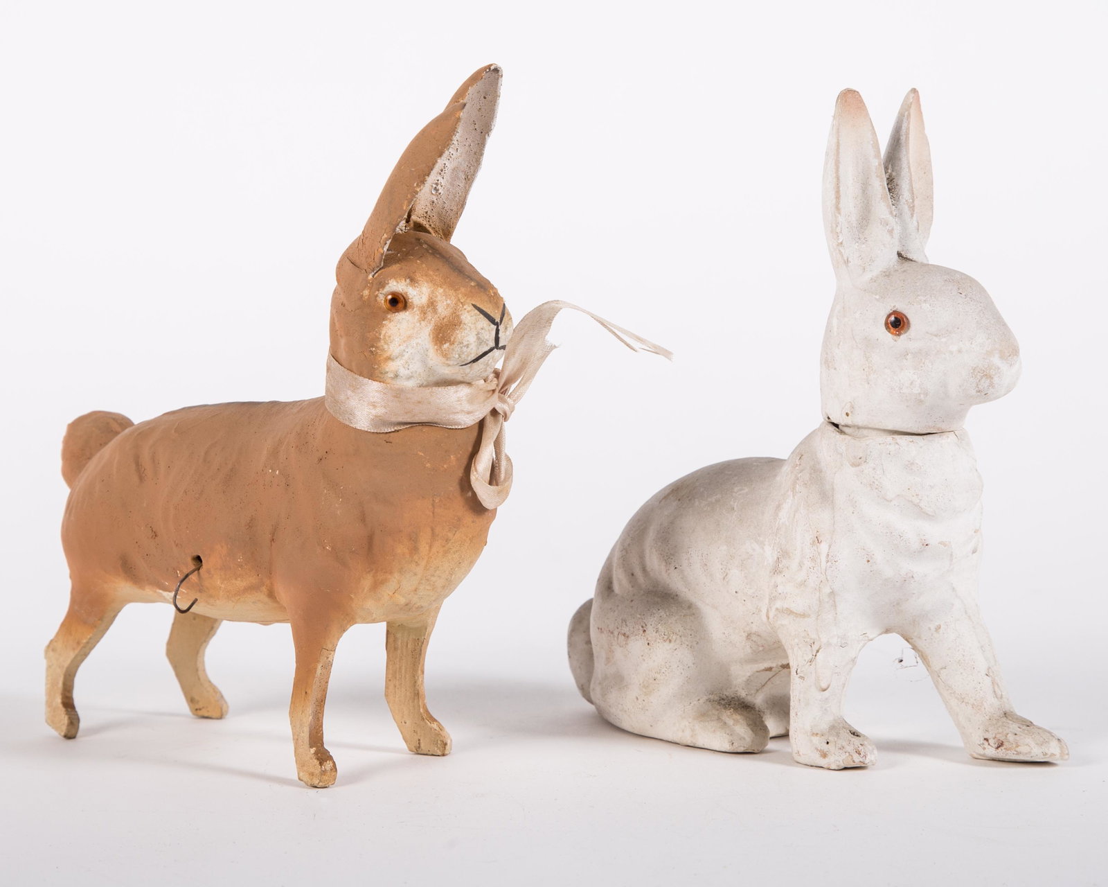 VINTAGE RABBIT CANDY CONTAINERS (2): Painted papier mache; white rabbit head fitting appears to have restoration; brown rabbit missing right eye and has wire through body; possibly pulled a cart at one time; overall minor paint loss; L-6