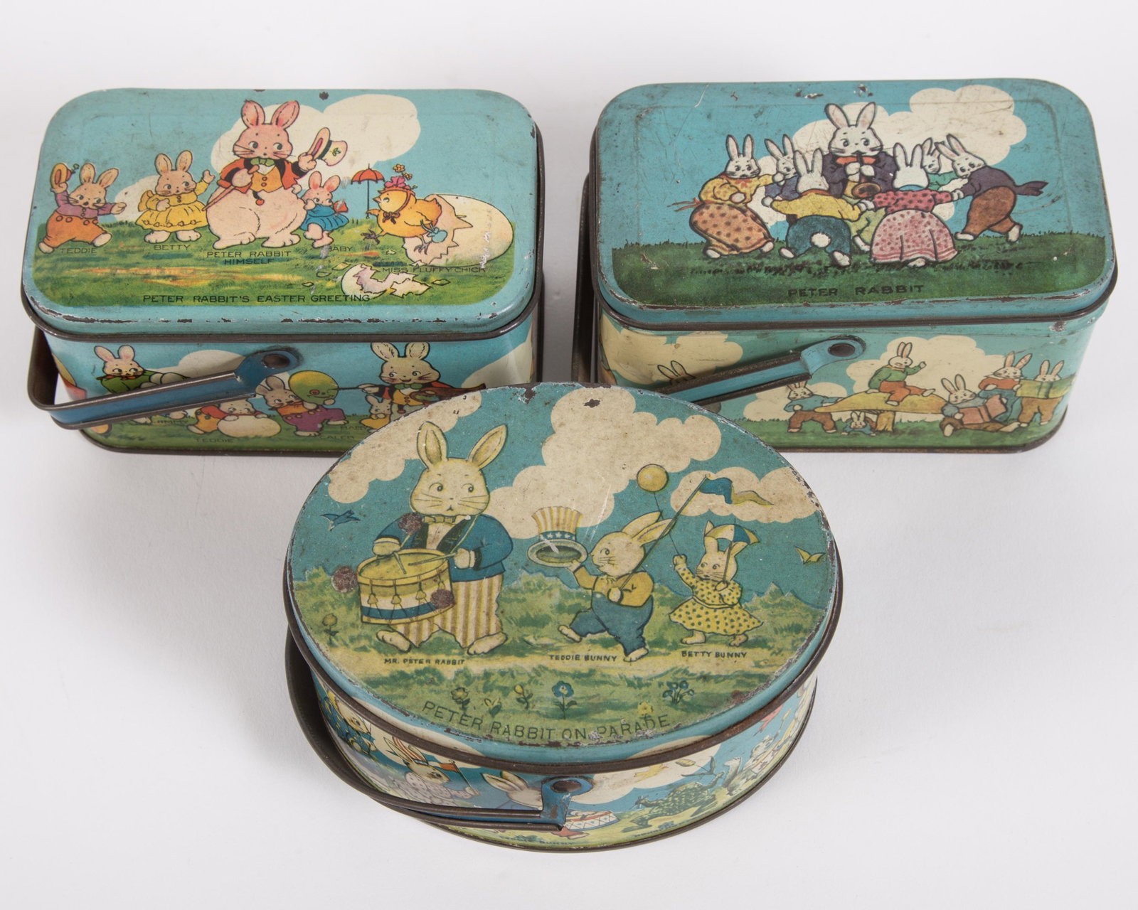 EASTER TINDECO CANDY BOXES (3): Tin litho; (1) Peter Rabbit's Easter Greeting; (1) Peter Rabbit on Parade; (1) Peter Rabbit; all stamped "Tindeco" on bottom; minor paint loss overall; some dents, scratches and fading; L-4 3/4", G-VG