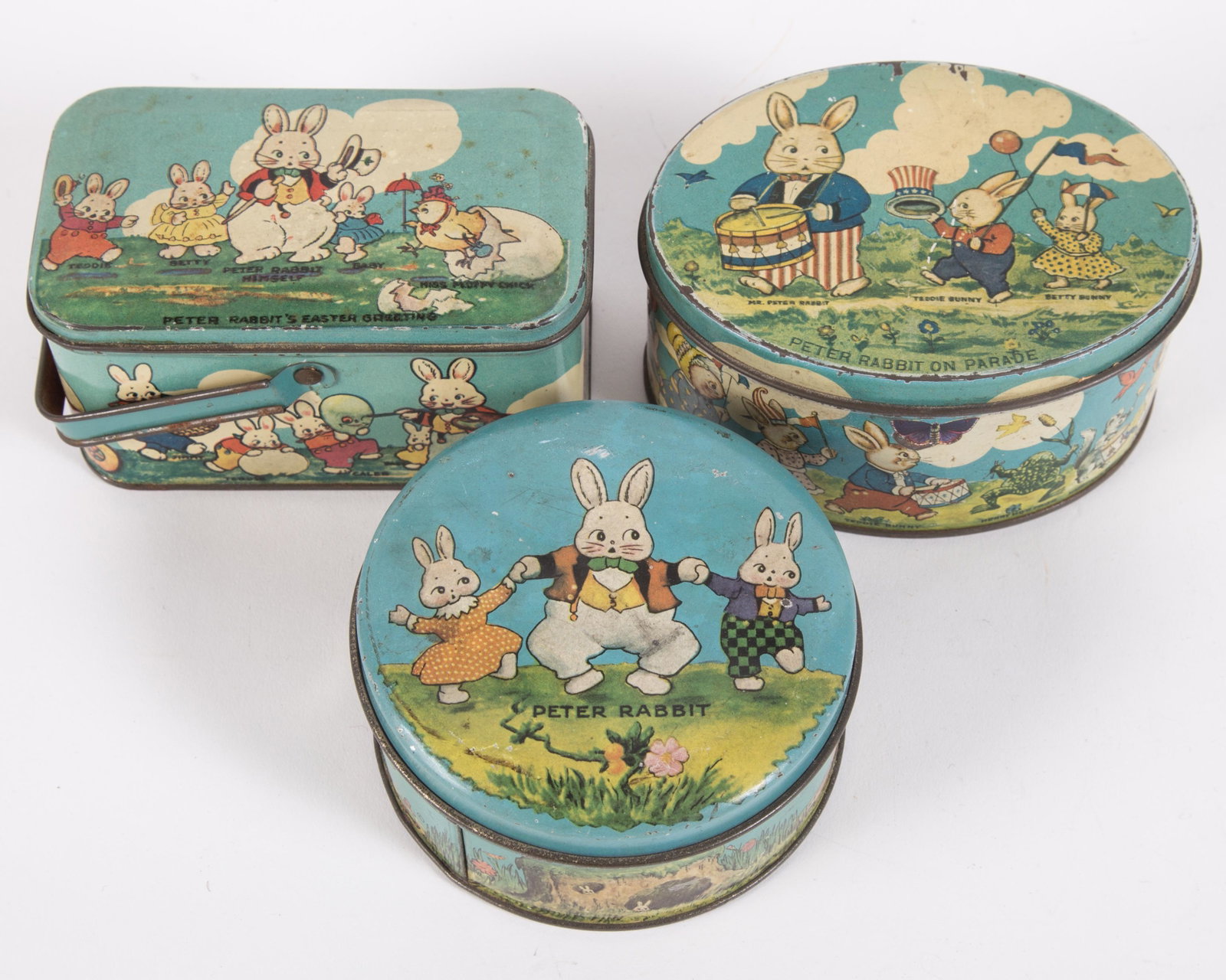 EASTER TINDECO CANDY BOXES (3): Tin litho; (1) Peter Rabbit's Easter Greeting; (1) Peter Rabbit on Parade; (1) Peter Rabbit; all stamped "Tindeco" on bottom; minor paint loss overall; some dents, scratches and fading; L-4 3/4", G-VG