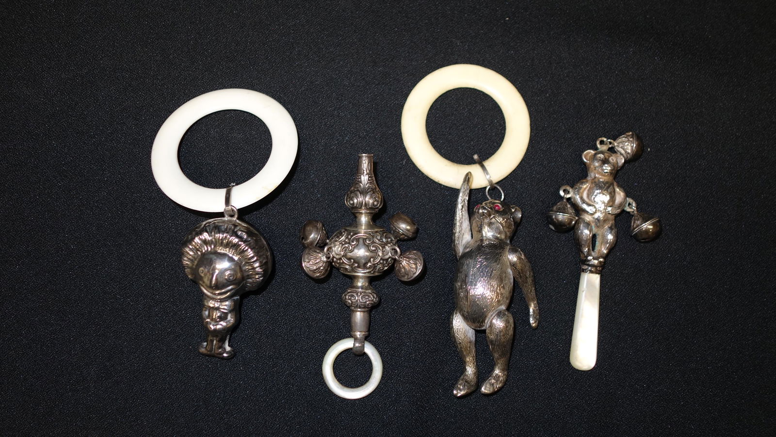 (4) BABY RATTLES: (1) Clown: W. A. England 4 1/2"; (1) bear: HVP & Co., moveable limbs, 5"; (1) repousse: marks illegible, mother of pearl ring, 3 1/2"; (1) bear with bells: C & N, 4", mother of pearl handle; sterling,