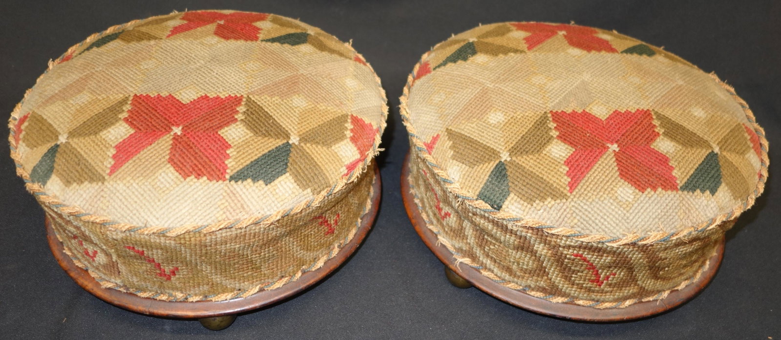 PAIR VICTORIAN FOOTSTOOLS: Needlepoint; wood bases with (3) brass ball feet; piping is frayed; thin areas in stitchwork faded; Dia.-12", F-G