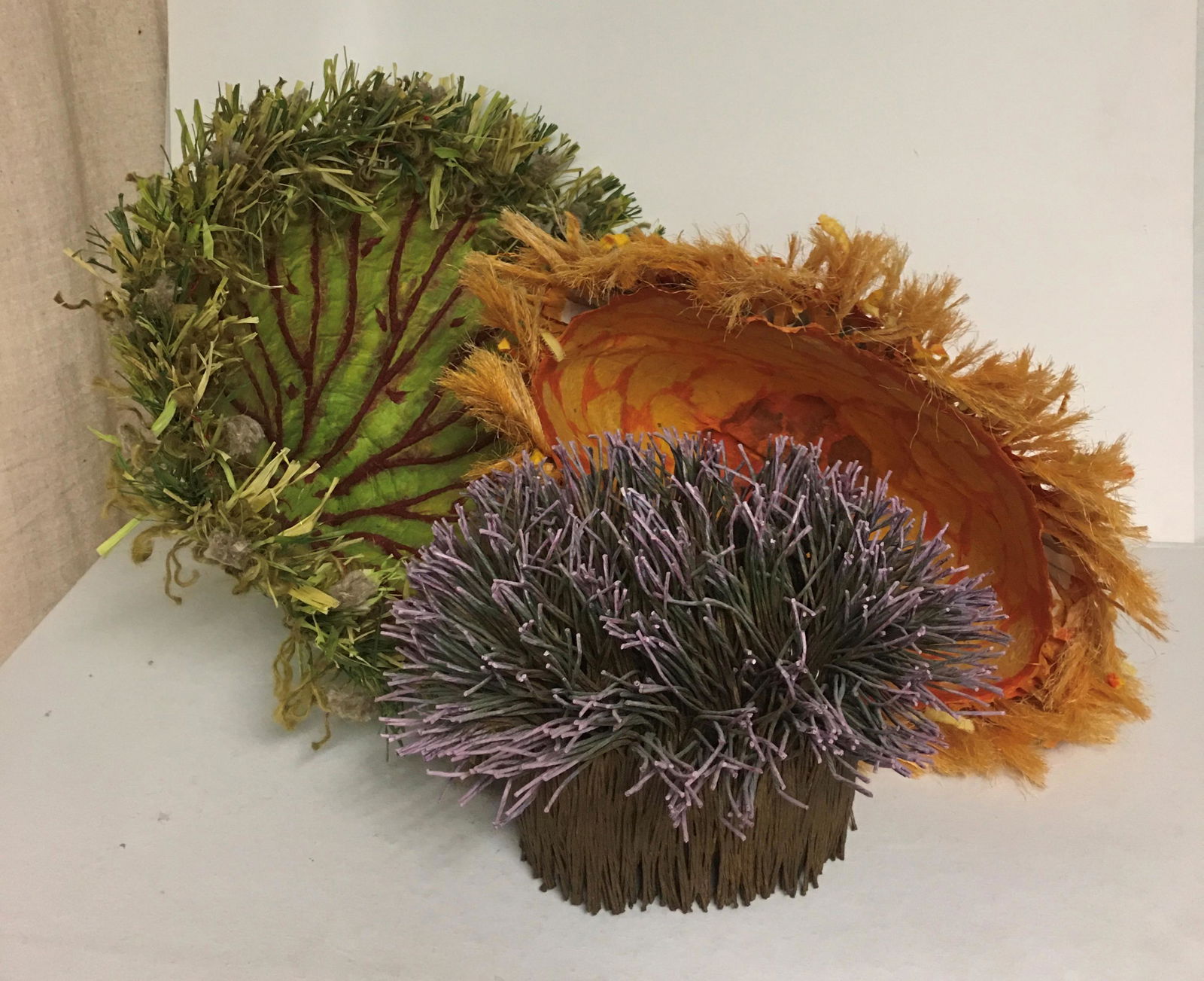 ARTISAN BASKETRY (7): (1) Grass basket with lid by Pavila; (1) lavender tipped, signed on bottom; (1) orange basket signed on bottom; (1) green with red veining, signed on bottom; (1) papier mache with figures hung from ri