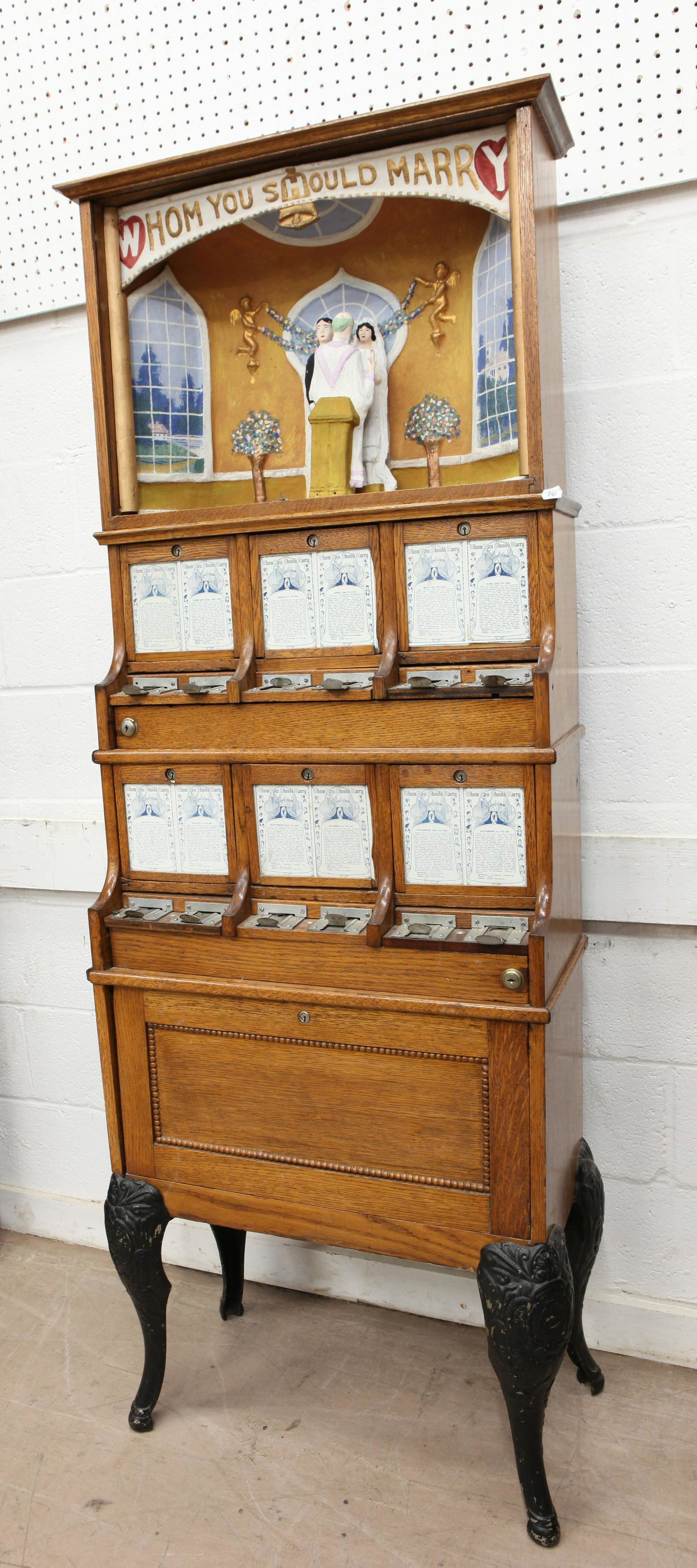 ARCADE COIN OPERATED AMUSEMENT: "Whom Should You Marry"; vintage coin operated; oak case with cast iron legs; diorama top has painted dimensional composition figures and background; (12) dated coin slots; 800-1000 (+/-) cards; repla