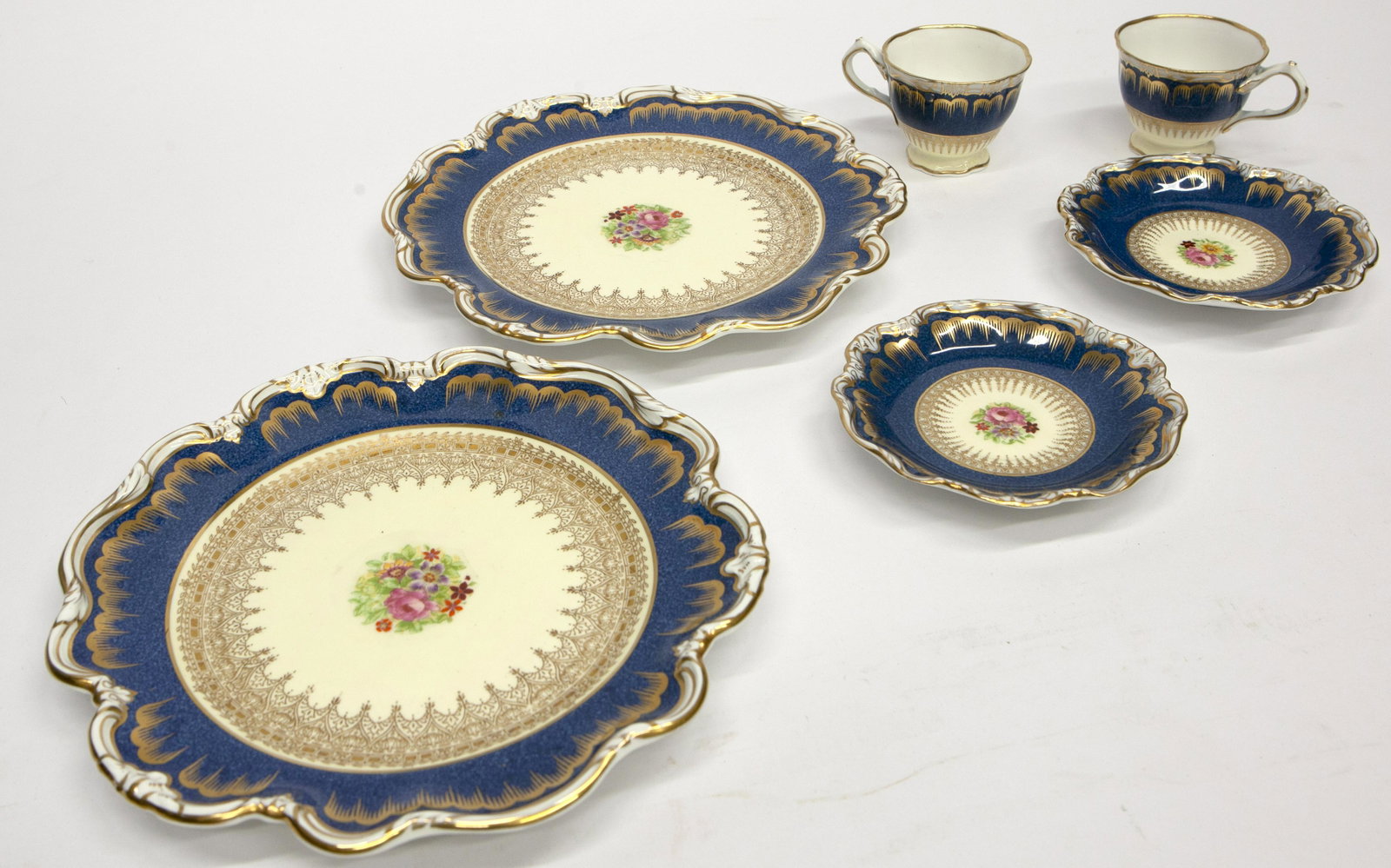 PORCELAIN DESSERT SERVICE: Crescent China; England; "George Jones and Sons"; ruffled edge with blue band and gilt decorated; floral transfer in center; (12) 9" plates; (9) demitasse cups and saucers; normal wear; VG-EX