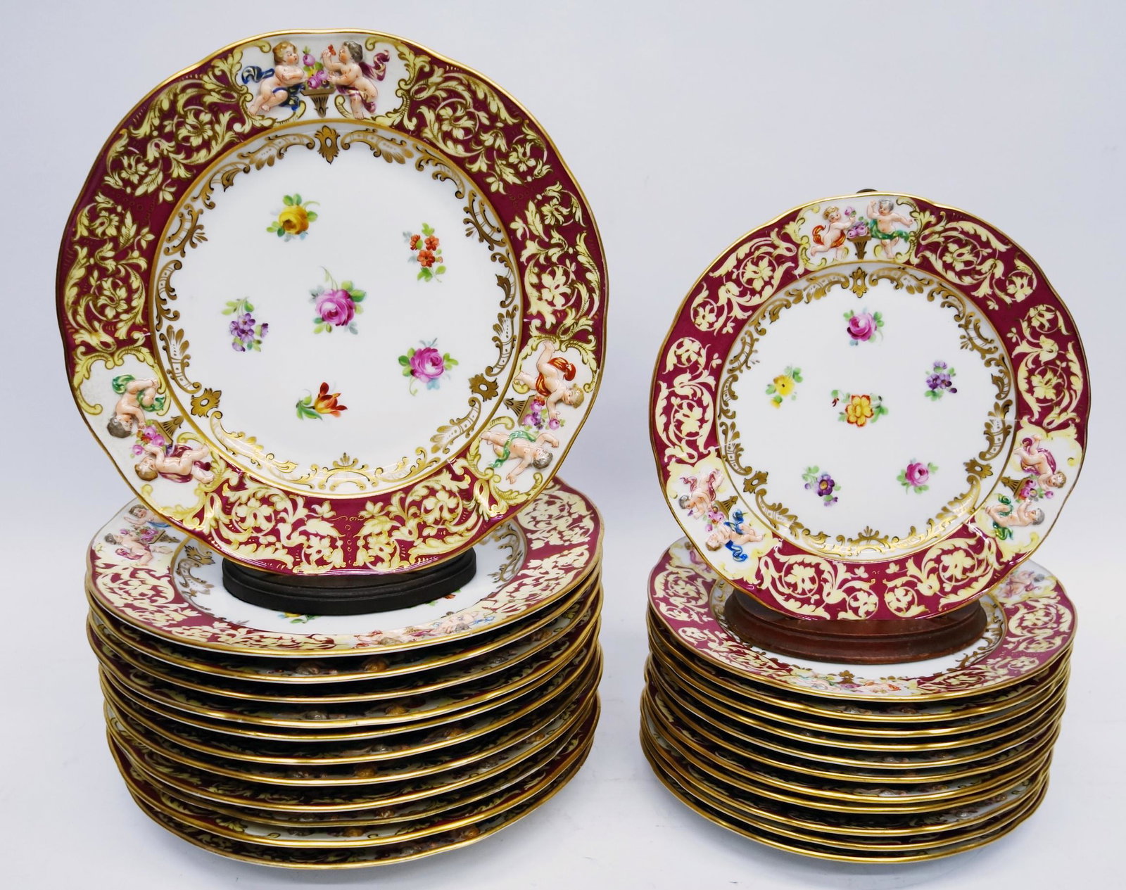 (24) CAPODIMONTE PLATES: Porcelain; floral center with embossed cherub border; maroon & gilt band; minimal wear; (12) Dia.- 8 1/2"; (12) Dia.- 10 1/2"; VG-EX
