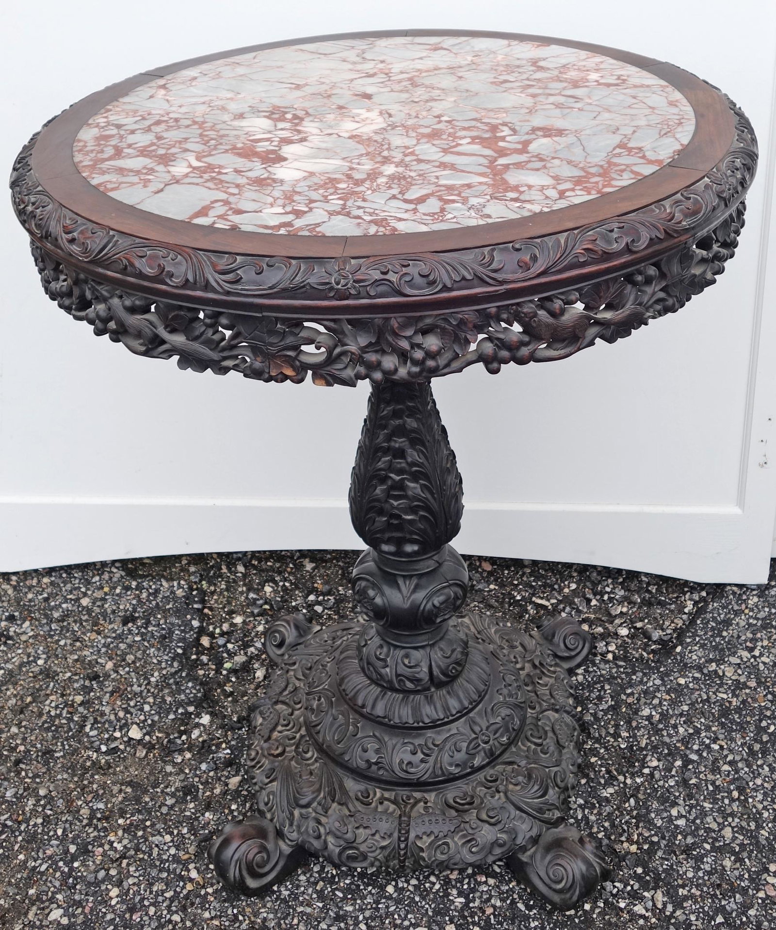 EASTERN CENTER TABLE: Carved teak, tilt top, marble inset top; elaborately carved apron; (1) section of carved apron damaged and pieces missing; H-38", Dia.-30", F-G
