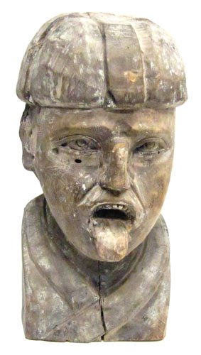 FOLK CARVED HEAD: Large carved head of man with tongue out; (1) piece wood with some gesso and traces of paint remaining; (1) large check in left side; some other minor splits and losses; H-19", G