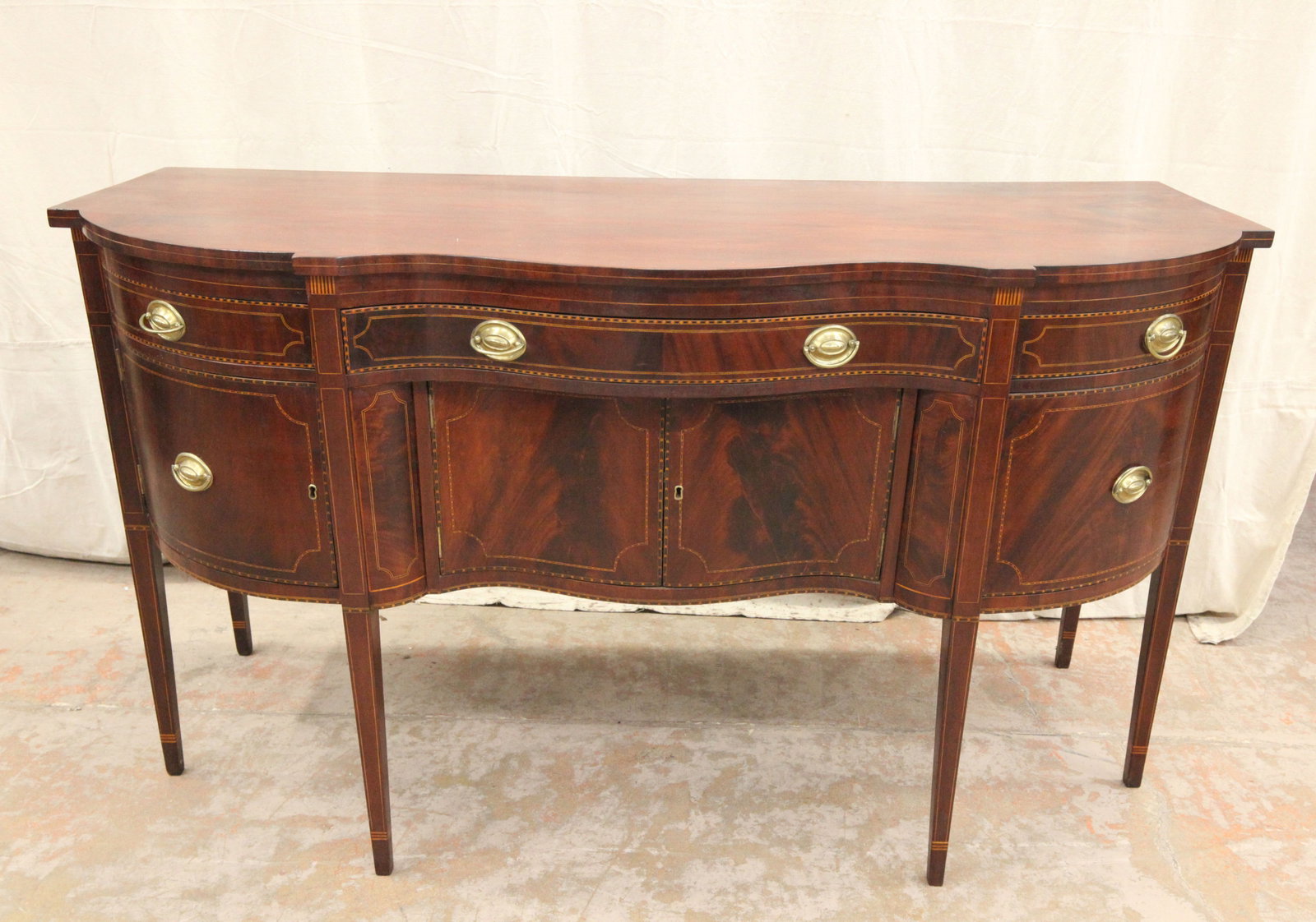HEPPLEWHITE SIDEBOARD: Mahogany; serpentine and shaped top, line and band inlay; right side liquor drawer, left side has door; some splitting in crotch grain; H-40", L-72", Depth 29", G-VG