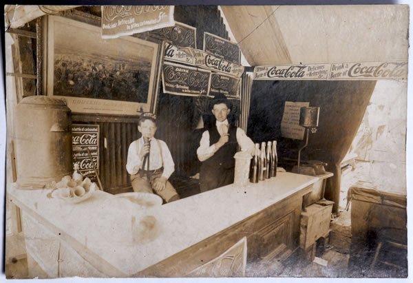 EARLY COCA-COLA PHOTOGRAPH: 4 1/2" x 6 3/4", circa 1934. Nice original print depicts a number of banners, several of which are quite unusual, as well as a Coca-Cola hat on the kid. Was removed from an old scrap book with some sl
