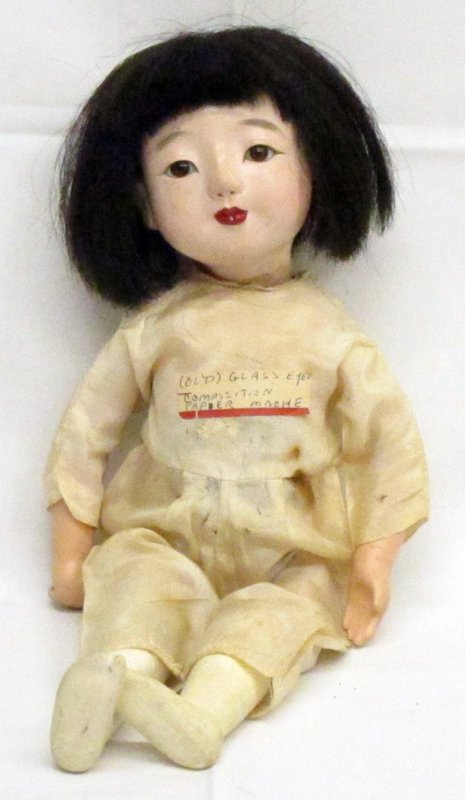 JAPANESE DOLL: Papier mache; glass eyes; real hair; hole in hand to hold doll; stomach squeaker (not working); head loose; rough base of neck; some chipping; minor scuffs; H-12", G