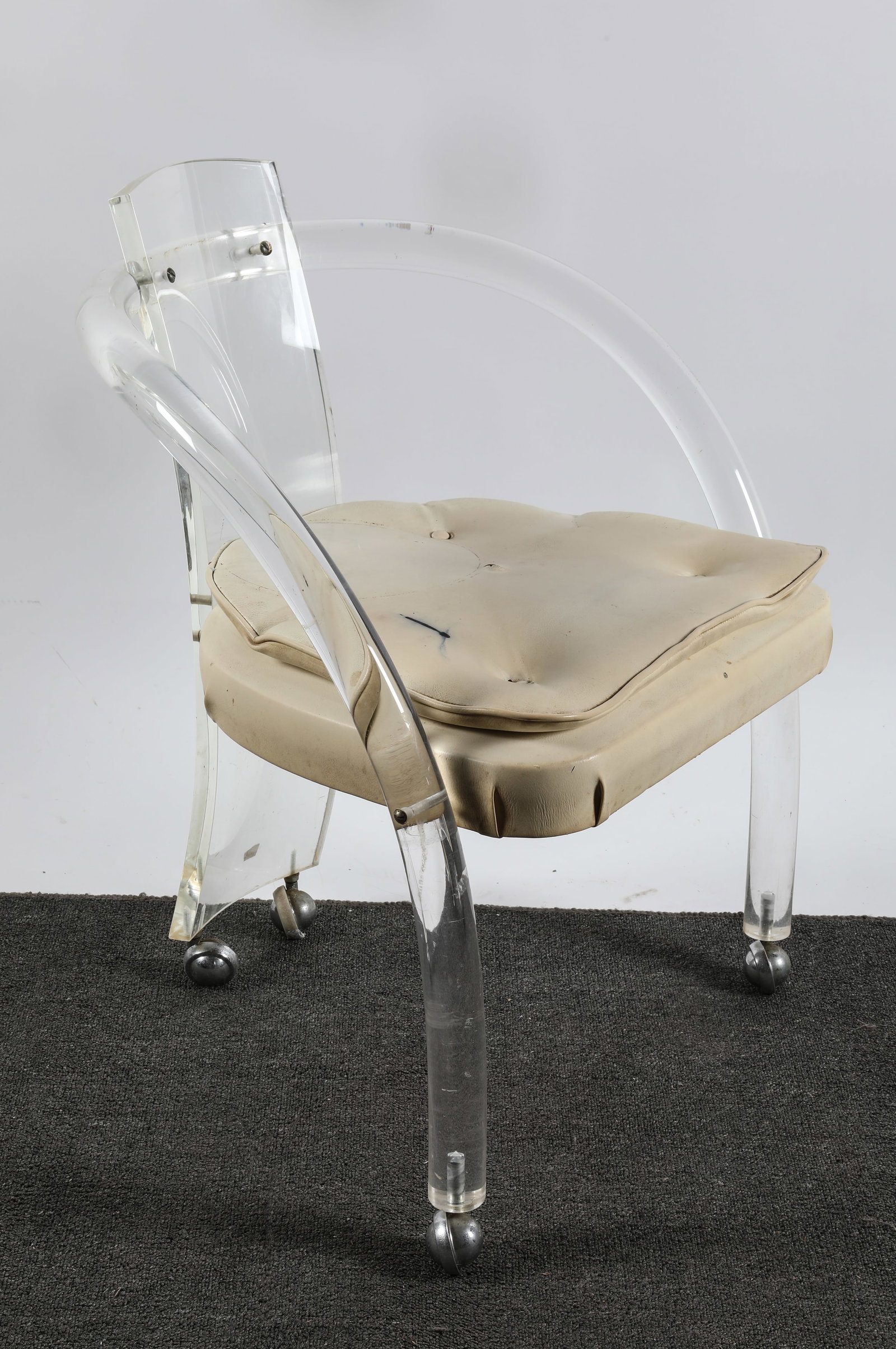 CHARLES JONES LUCITE CHAIR: Designed for Hill; Lucite with vinyl cushions; on rollers; H-30"xW-24"; numerous scratches, seat missing buttons and has ink stain, F
