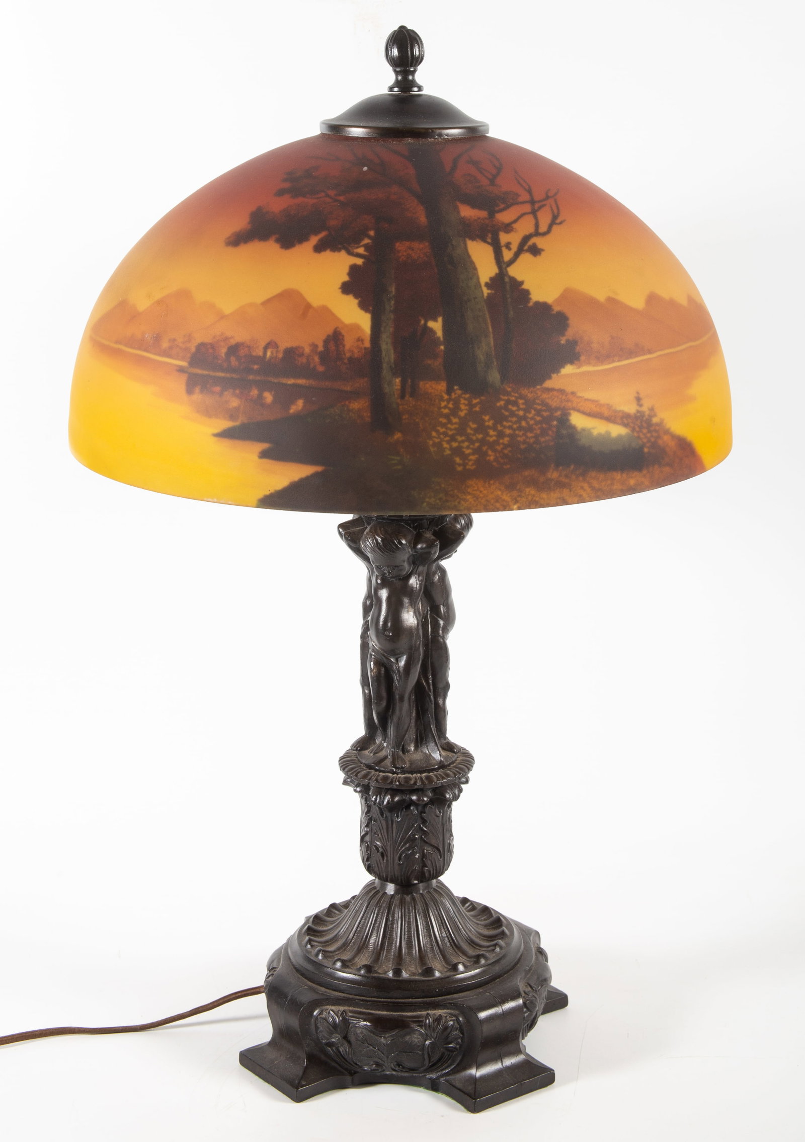 RETRO SCENIC SHADE TABLE LAMP: Reverse painted landscape shade; patinated metal base with cherubs; lamp height 25 1/2" - shade diameter 16"; normal wear, G-VG