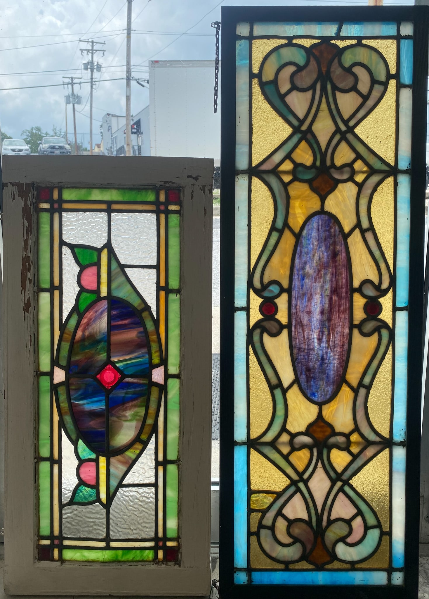 (2) LEADED AND STAINED GLASS PANELS: Both probably transoms with wood frames - (1) geometric scrolls, center oval medallion, and (2) jewels, 13"x40"; (1) geometric and floral pattern with leaf, some ripple glass, 14"x30"; normal wear, G-
