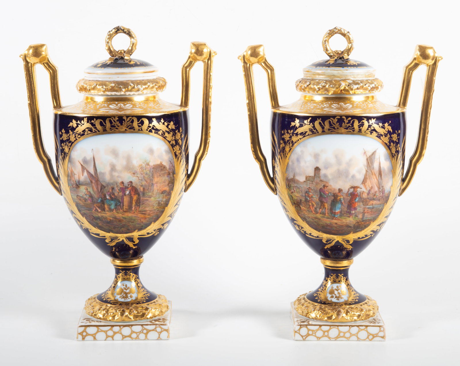 PAIR OF DRESDEN PORCELAIN URNS: Painted porcelain covered urns with exaggerated handles; (4) different detailed oval scenes with numerous figures, boats, etc.; H-11 1/2"; some ribbon loss on lids, (1) lid has hairlines, G-VG