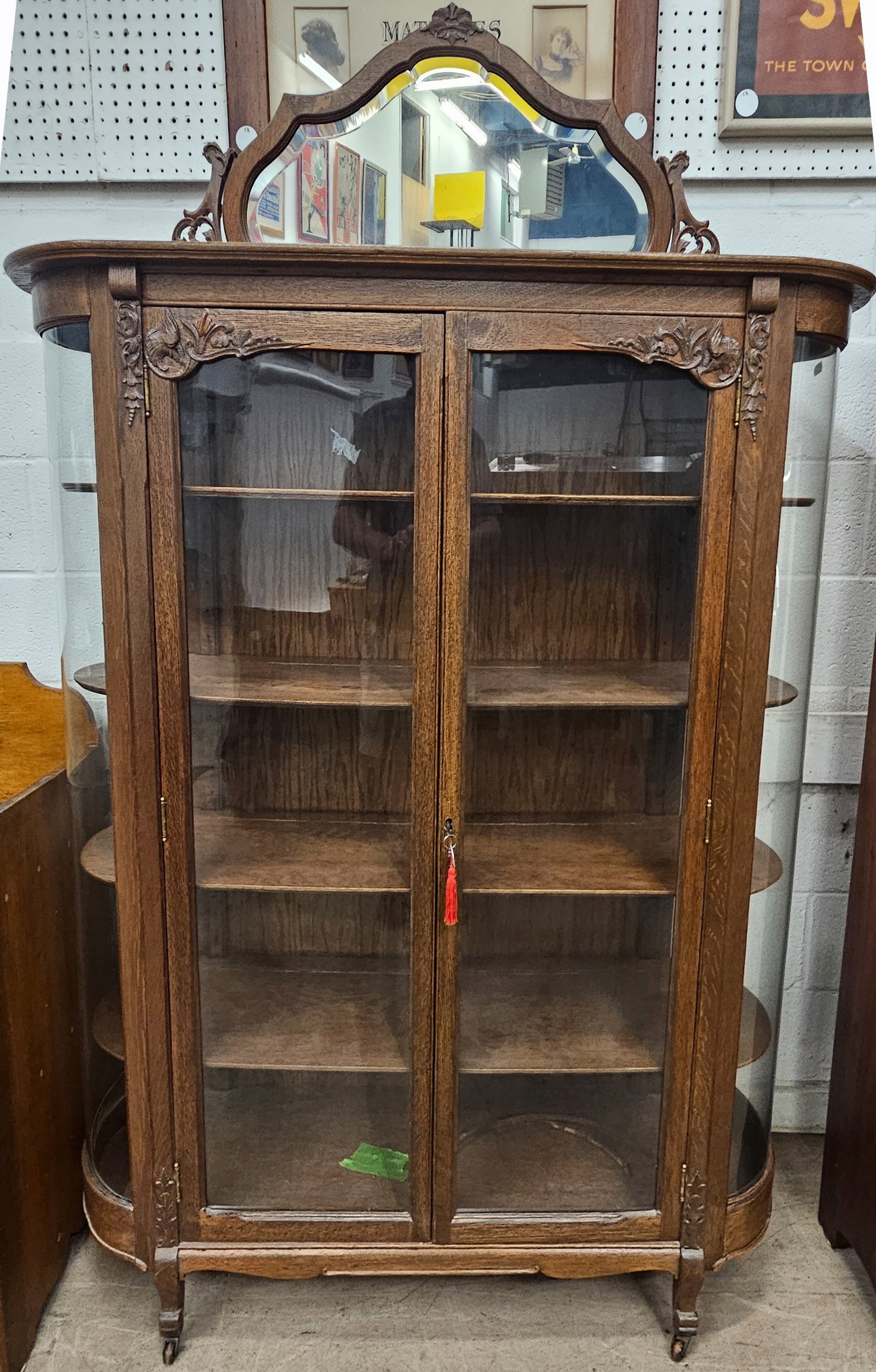 VICTORIAN OAK CHINA CABINET: Beveled mirror crest, flat doors, curved side glass, ornate carving on door posts and doors, original finish, H-76"xW-50", needs (3) curved molding trim reinstalled, G-VG