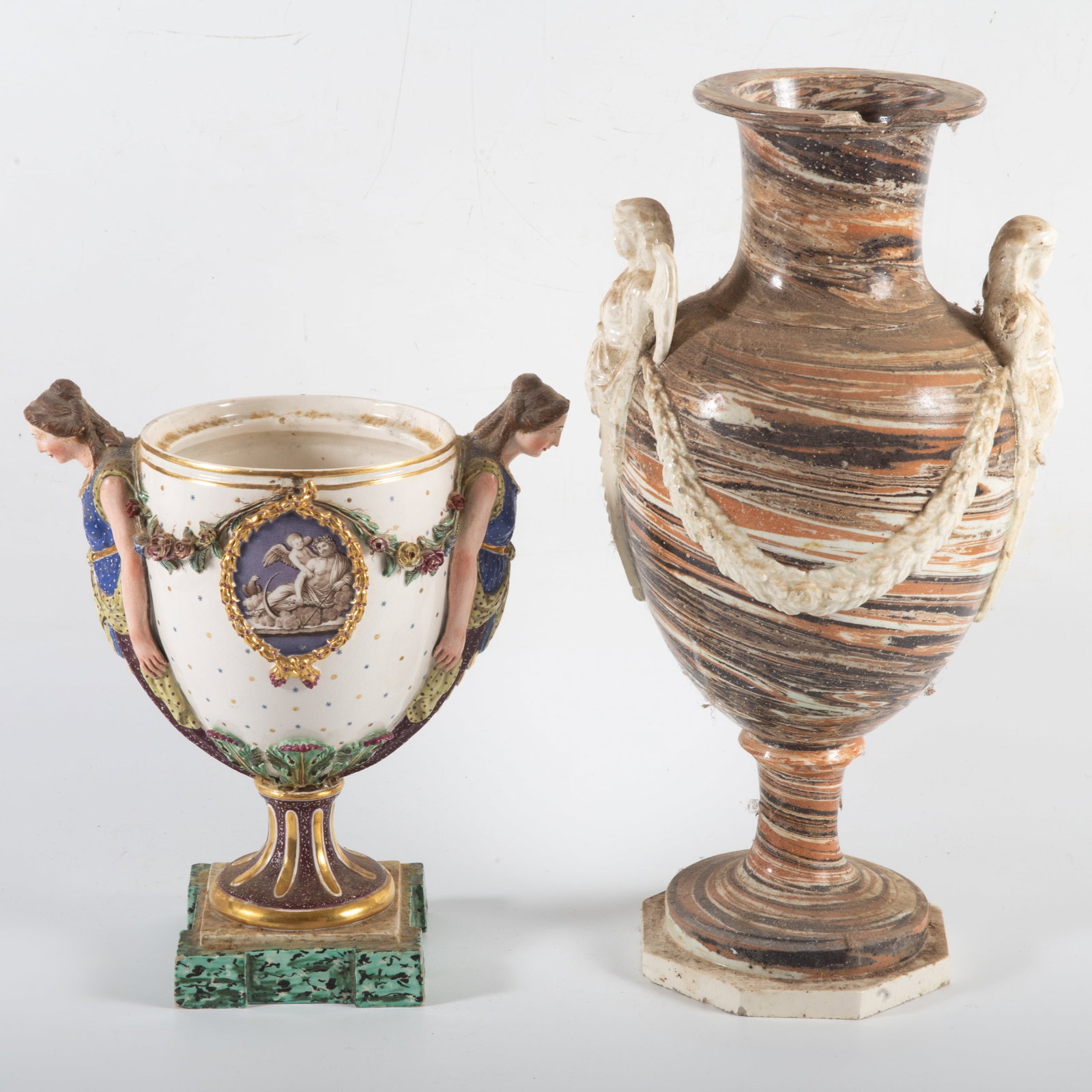 (2) EARLY PORCELAIN / CERAMIC URNS: (1) Tall marbled urn with applied drapery and angel handles; damage and losses- P; (1) porcelain urn with caryatid handles- painted porcelain classical medallions, floral drapery, missing lid, some mi