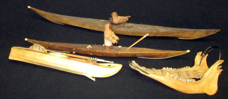 ESKIMO MODEL KAYAKS (3): Together with jaw bone dog sled, (3) hide covered kayaks, (2) having figures with carved wood bodies, some pieces missing, dog sled damaged; longest L-30", F-G