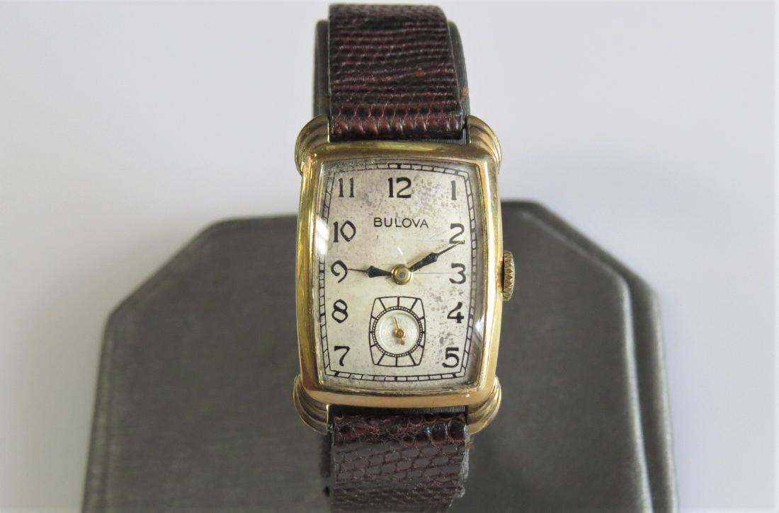 Vintage Bulova Mens Watch: Vintage mens Bulova wrist watch. Rectangle shaped case. 10KT Yellow gold plated case. Stainless steel back. Brown genuine lizard band with 5 adjustable wrist sizes. 19x25mm case - 11mm band width. 12.