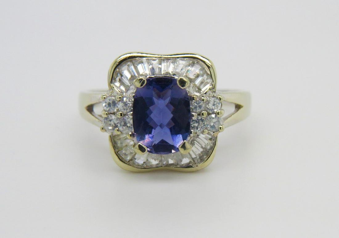 10K White Gold Tanzanite and Diamond Ring: Stamped 10K white gold, Tanzanite and diamond ring. Center cushion checkerboard cut tanzanite is set into four prongs and measures approximately 1.35 cts. Accented with a diamond halo of baguette and