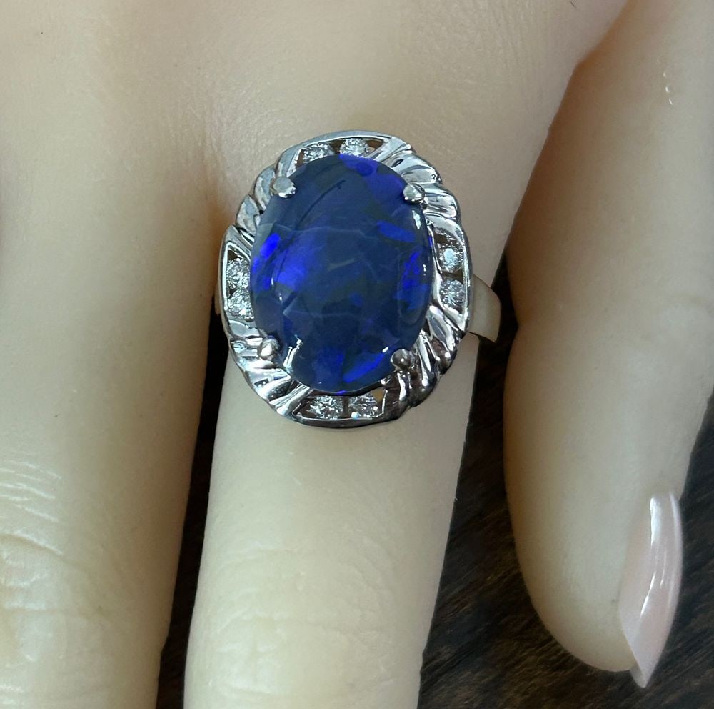 Diamond and Black Opal Ring: S/9-MSSS Commanding attention, this magnificent ring features a striking oval-cut black opal, with dark blue body tone. The dramatic central opal is elegantly framed by a pairs of brilliant diamonds,