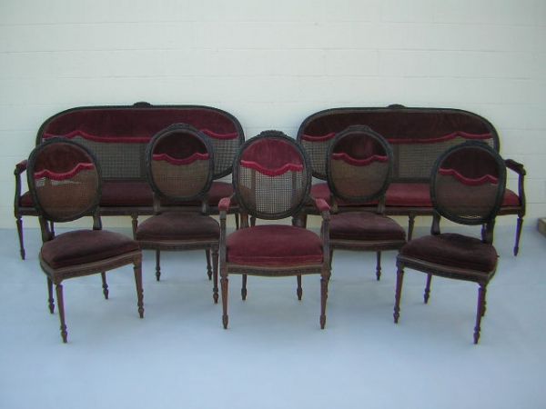 7 Piece French Style Parlor Set C 1910-1920: Parlor set comprised of a pair of settees, four side chairs and one arm chair. Each with carved wooden frames with woven wicker inserts to backs and seats. Applied plaster trim molding. Upholstered ar