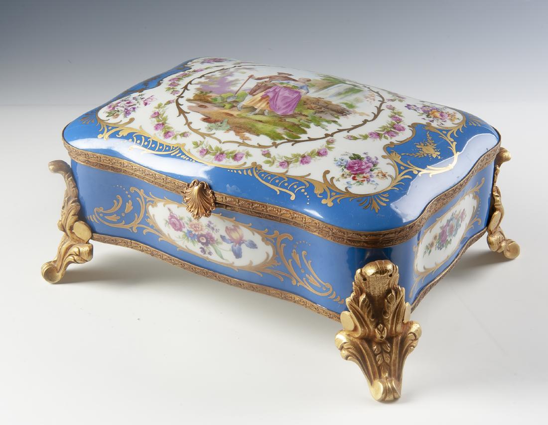 Large Sevres Porcelain Dresser Box: DESCRIPTION: Large blue Sevres porcelain dresser box. With bronze fittings, gilt accents and romantic scene to lid. Floral decoration to sides and interior. Bottom with Sevres mark over "France". MEAS
