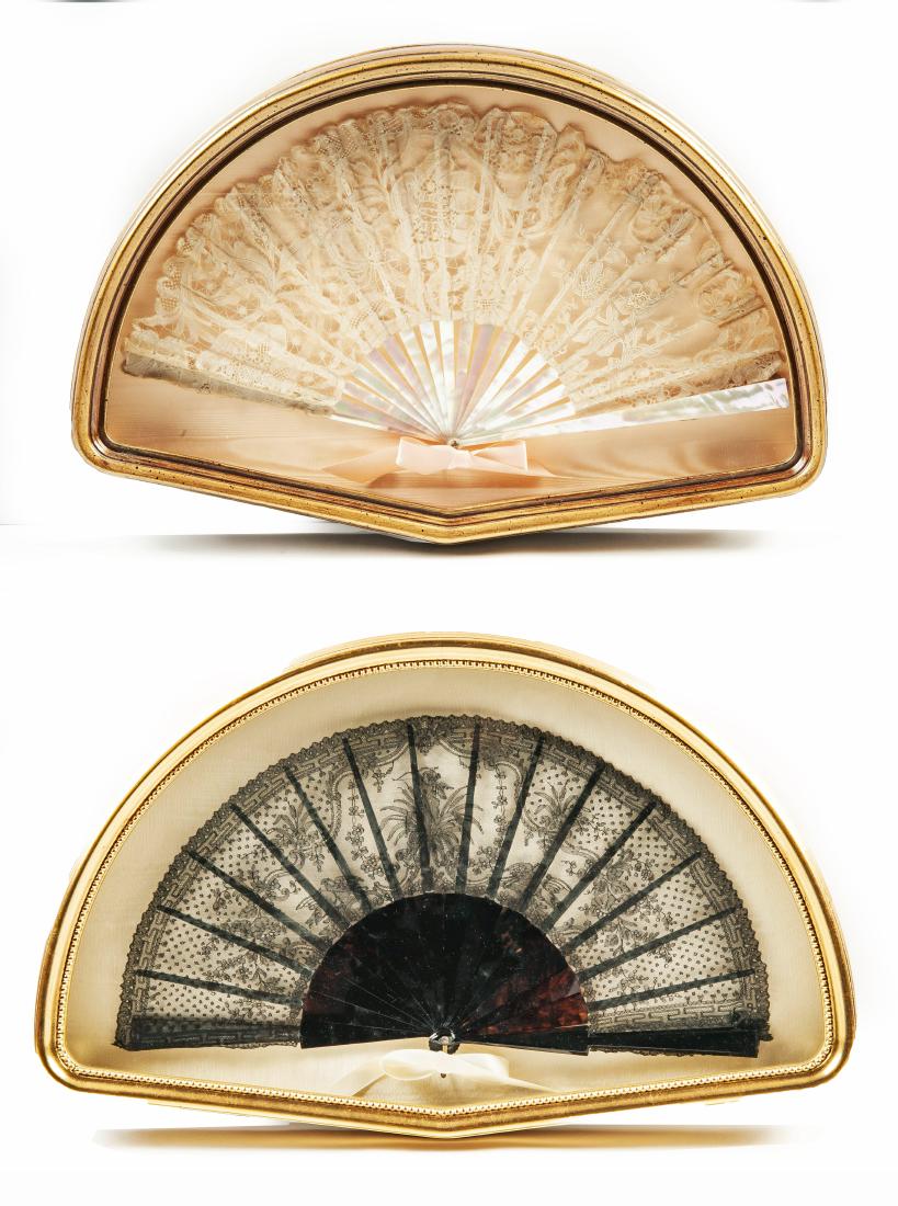 2 Framed Folding Fans: DESCRIPTION: Two framed folding fans. Includes: 1) Cream colored lace leaved fan with mother of pearl sticks, ribs, and guard. Metal closure clasp with pink ribbon. Approximately 18" x 10". Discolorat