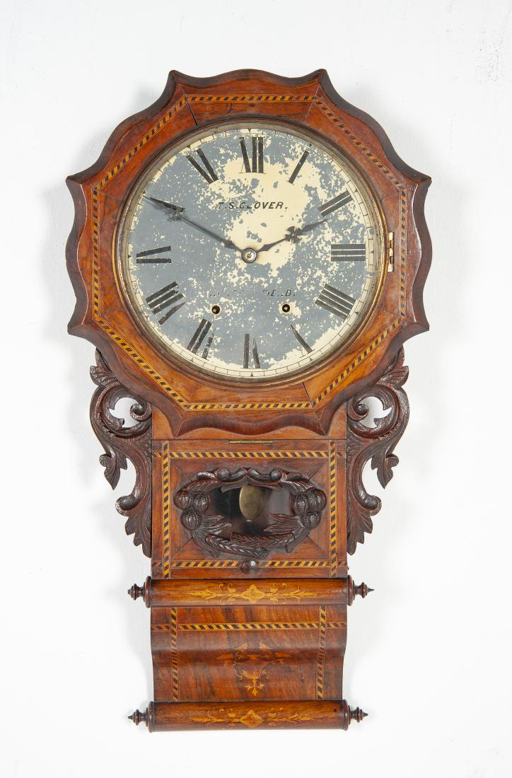 T. S. Clover Inlaid Wall Clock: DESCRIPTION: T. S. Clover inlaid wall clock. Painted tin dial. Roman numerals. Time and strike movement. Elaborately carved and inlaid mahogany case with acorn and foliate motifs. Includes key and pen