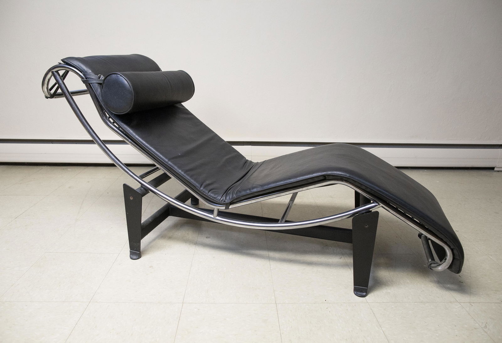 Lounge Chair in the Manner of Le Corbusier: DESCRIPTION:Black leather and chrome lounge chair in the manner of Le Corbusier LC4. Curved chair rotates on axis in base. With attached bolster. MEASUREMENTS: 21" wide x 60" deep x 32" high at back.