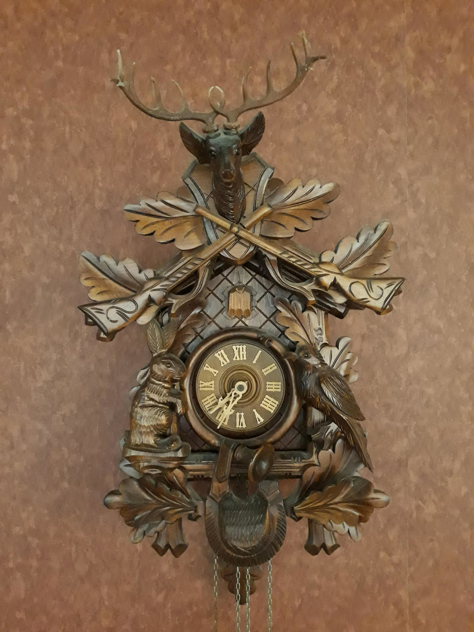 Black Forest Cuckoo Clock: Hunter style with rabbit, bird, horn, stag, rifle, oak leaves. Pine cone weights. With COA label to back. 12" wide x 17"high. Running.
