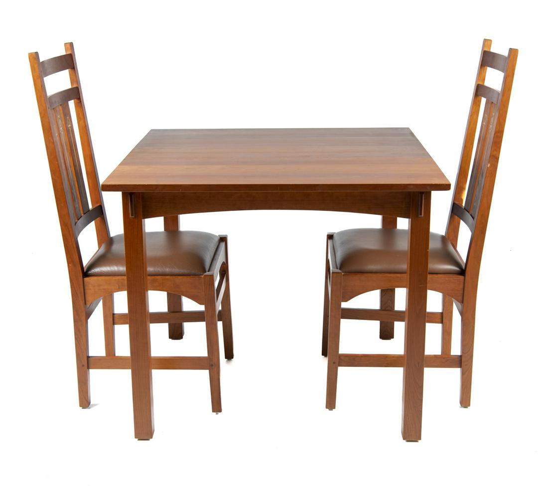 Harvey Ellis Stickley Cherry Table & 2 Chairs: DESCRIPTION: Harvey Ellis Stickley mission style cherry table with two chairs. Chairs with leather seat upholstery and inlay decoration to vertical back slats. Table with glass top. Labeled on bottoms