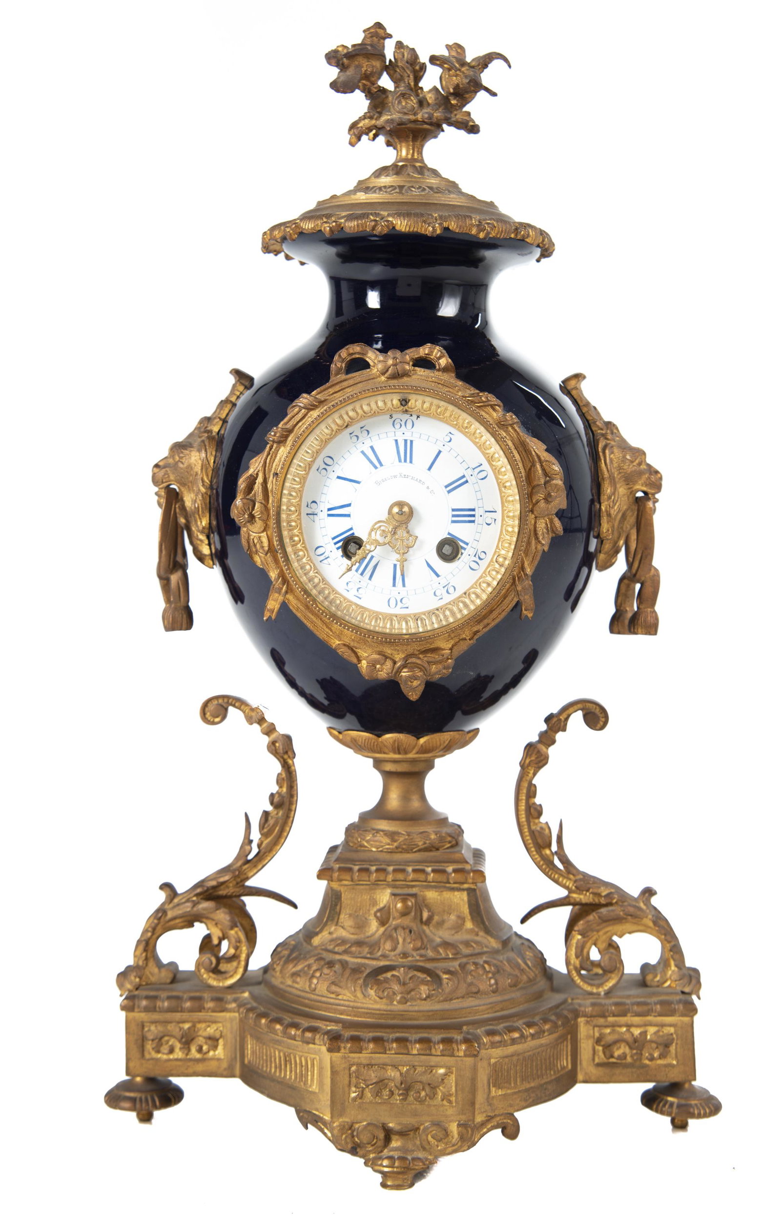French Brass & Porcelain Mantle Clock: DESCRIPTION: French brass and blue sevres vase mantle clock. Louis XVI style. Porcelain dial with Roman numerals marked "Bigelow Kennard & Co.". Time and strike movement. Decorated with lions heads an