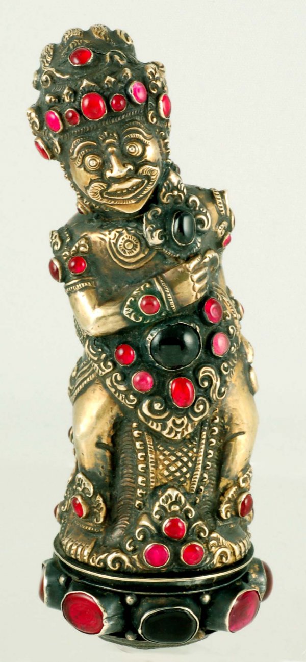 Tibetan/Nepalese Jeweled Brass Figure of Kubera: DESCRIPTION: A Tibetan or Nepalese brass plated figure probably of Kubera with inset red glass stones of various sizes and shapes. A hole in the base suggests the figure was the top of another item, p