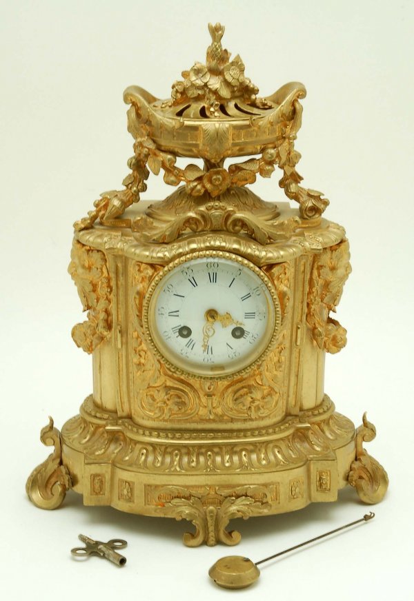 French Ormolu Mantle Clock: DESCRIPTION: A French ormolu mantle clock. Case flanked on each side by a green man and surmounted by a swagged urn of flowers with removeable cover. Porcelain dial with gilt hands and beveled glass c