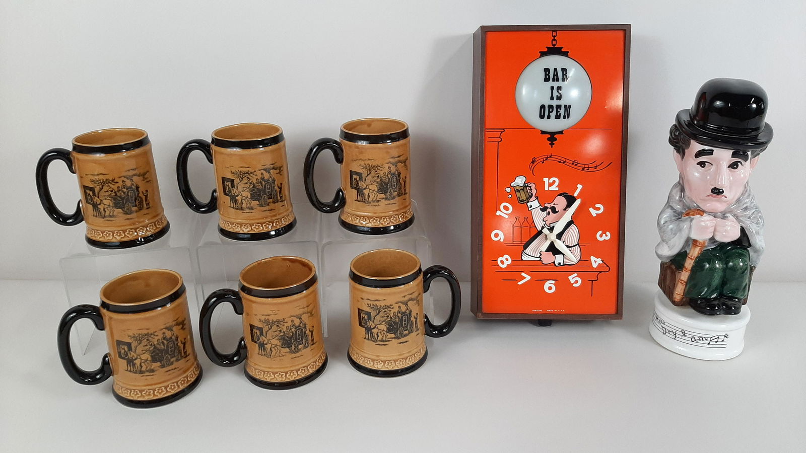 6 Mugs, Barnett Clock, and Chaplin Decanter: Mugs made in occupied Japan. "Bar is Open" clock made by Spartus. Working. "How Dry I Am" Charlie Chaplin Decanter spins and plays music. Mugs: 3¾" diameter X 4½" high. Clock: 7" wide X 2¼" deep X